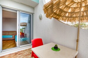 Ein Balkon mit einem Tisch, einem roten Stuhl, einer Topfpflanze und einem Strohdachschirm.