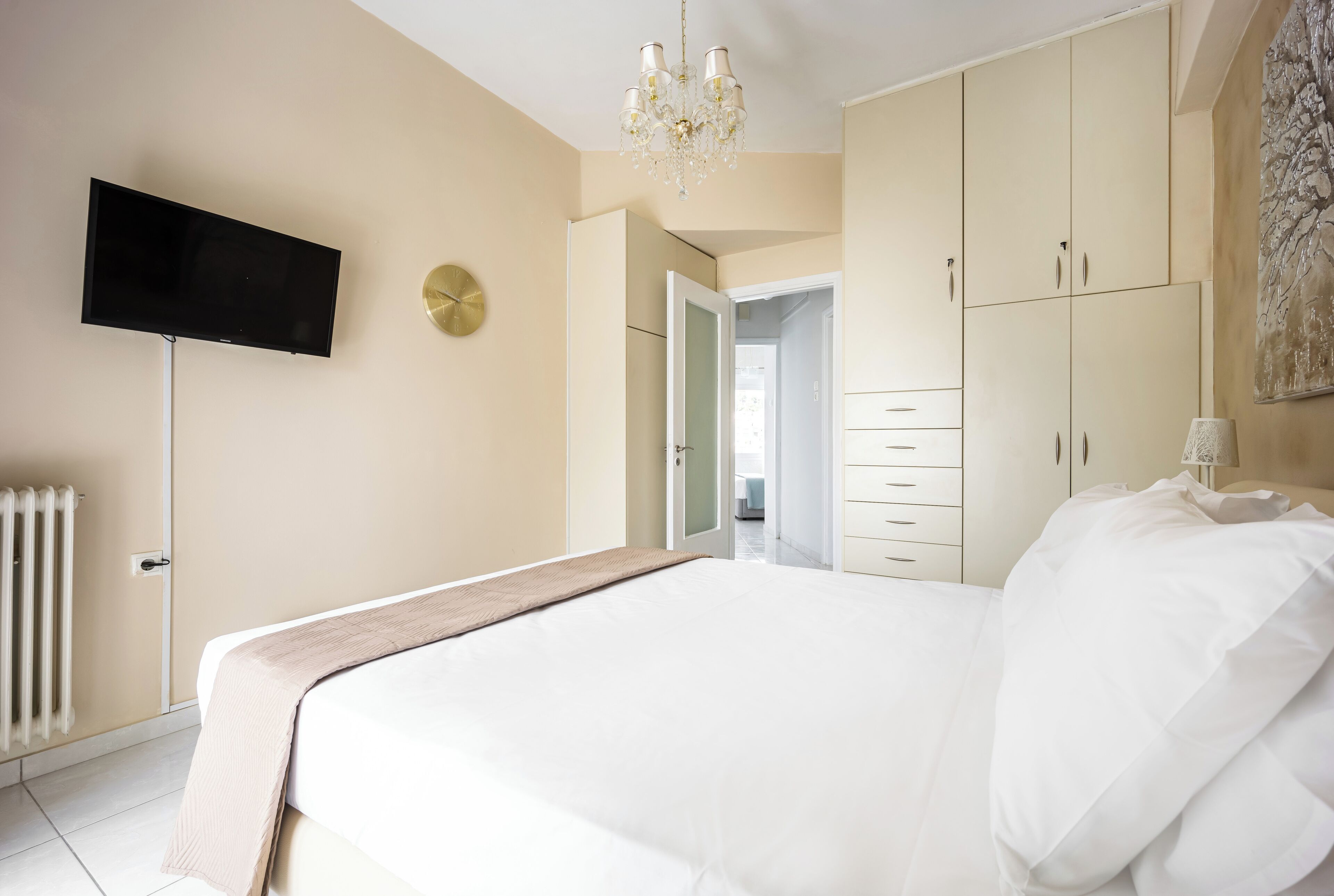 A bedroom with a bed, a television mounted on the wall, a chandelier, and a wardrobe.