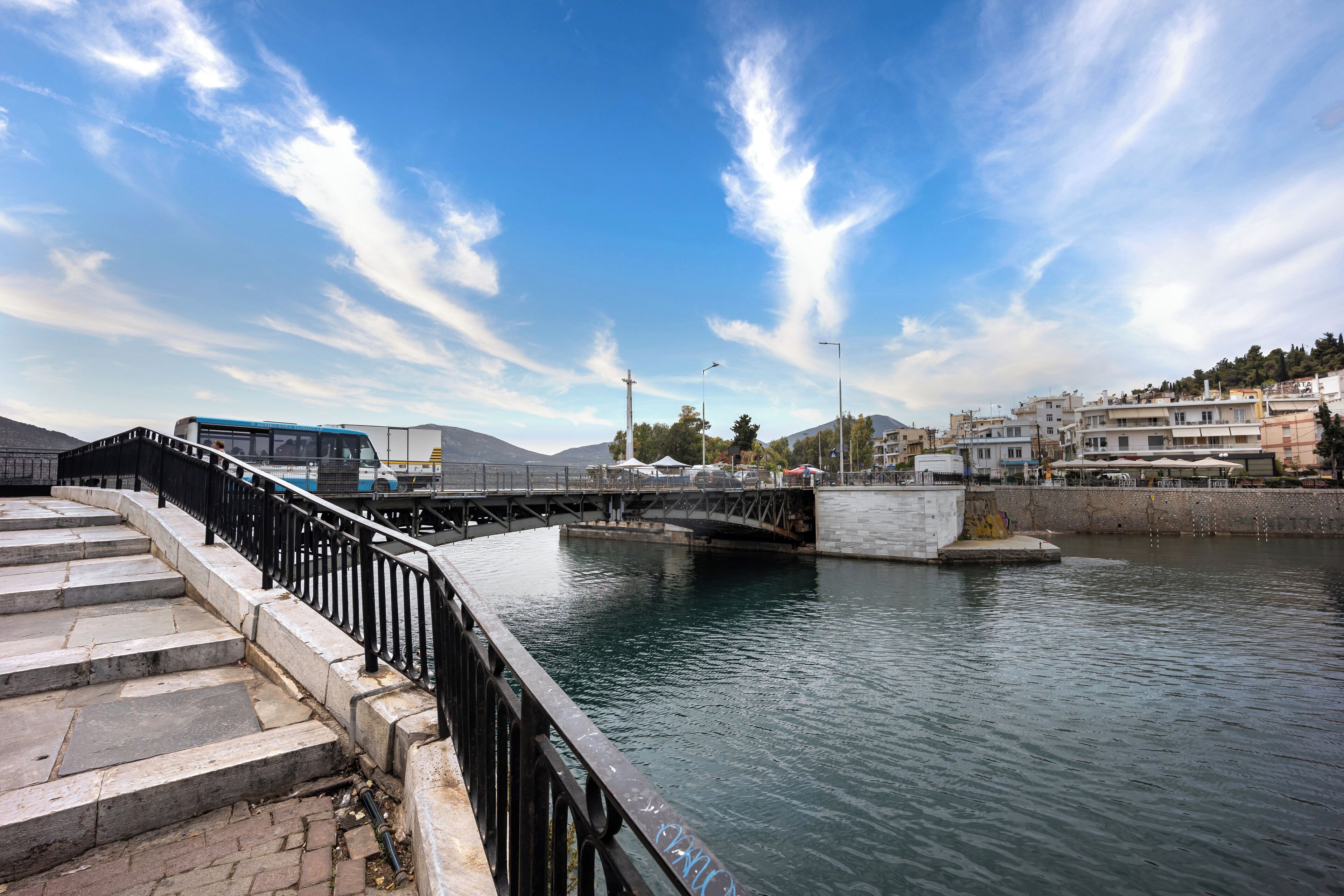Un pont sobre un riu, amb un autobús i edificis al fons.