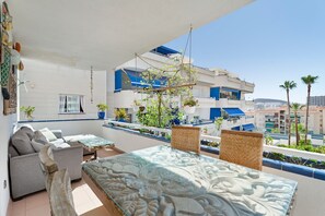 A balcony with a sofa, a glass-top table, and hanging plants.