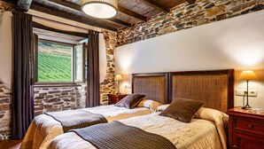 Ein Schlafzimmer mit zwei Betten, Steinwänden, Holzbalken und einem Fenster mit Blick auf grüne Hügel.