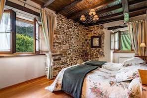A bedroom with a stone wall, wooden floor, and a bed with floral bedding.