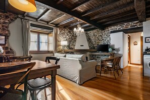 A rustic interior with a stone wall, wooden beams, a sofa, a dining table, and a washing machine.