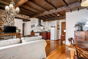 A living room with a sofa, a television, a chandelier, and a kitchen in the background.