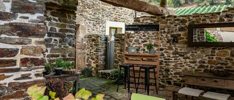 Un patio al aire libre con paredes de piedra, muebles de madera, una zona de bar y plantas en macetas.