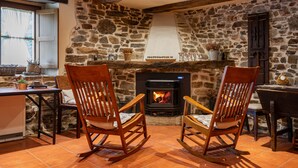 Ein rustikales Interieur mit einer Steinwand, einem Kamin, zwei Schaukelstühlen und einem Tisch mit Topfpflanzen.