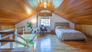 A bedroom with a sloped ceiling, wooden flooring, a bed, a chair, and a window. - Holiday Home 'O Axouxere' with Mountain View, Private Terrace and Wi-Fi (Feira do Tres)