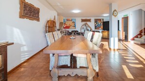 A dining area with a long wooden table, upholstered chairs, and a large painting on the wall. - Holiday Home 'O Axouxere' with Mountain View, Private Terrace and Wi-Fi (Feira do Tres)