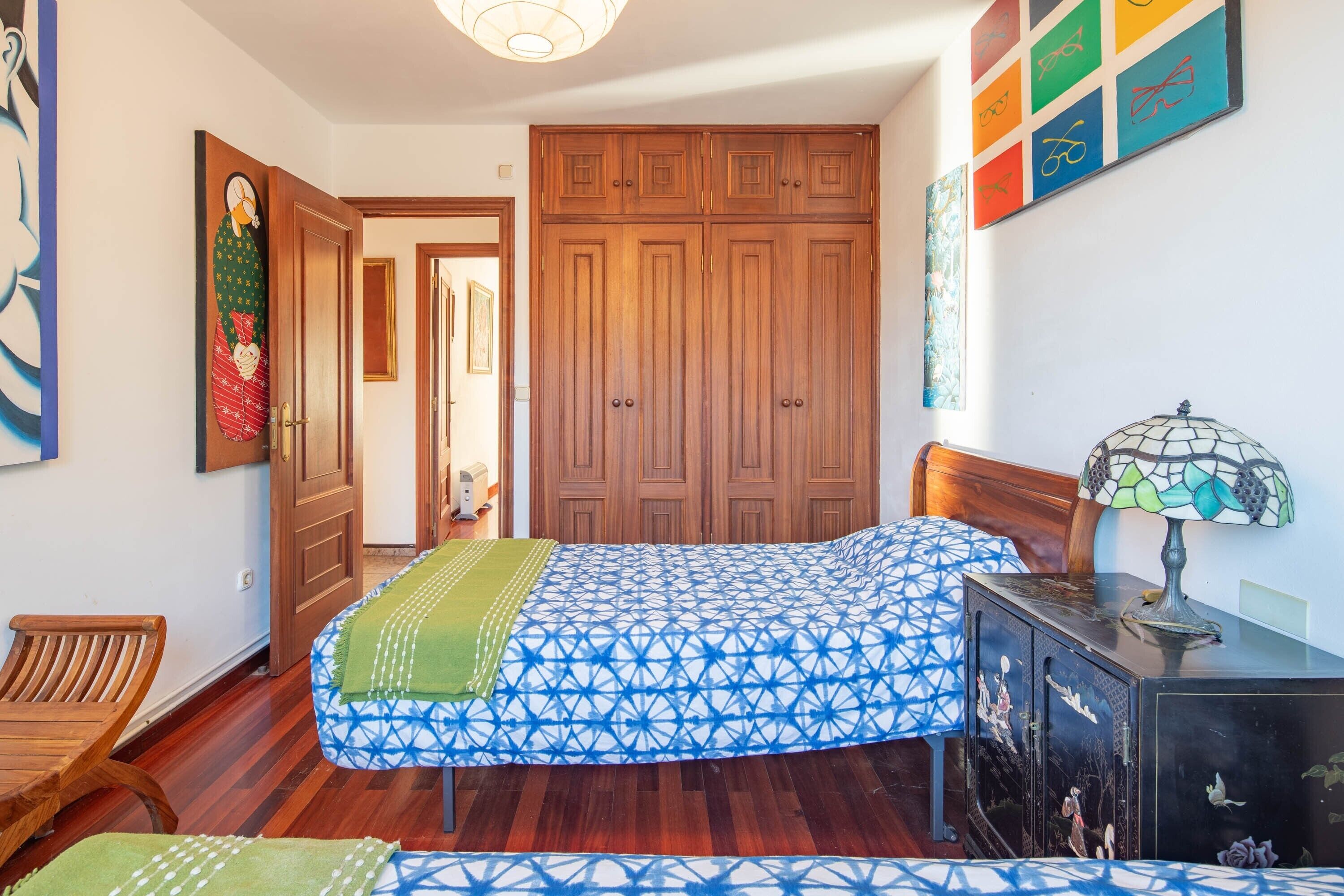 Un dormitorio con cama, armario de madera y escritorio con lámpara.