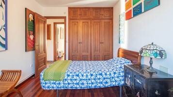 Un dormitorio con cama, armario de madera y escritorio con lámpara.