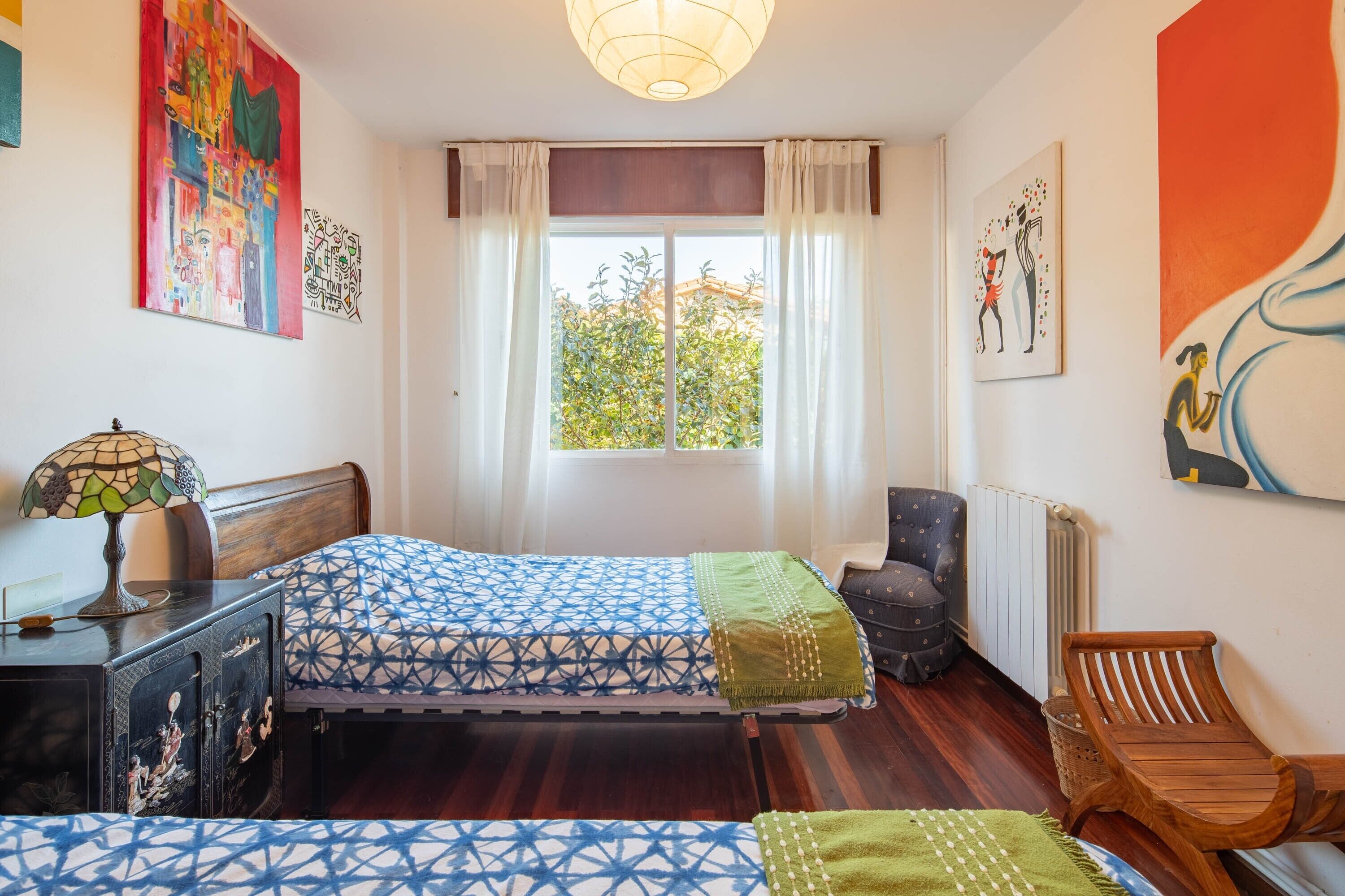 Ein Schlafzimmer mit Bett, Sessel, Schreibtisch und Bildern an den Wänden.
