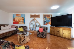 Uma sala de estar com sofá, poltronas, mesa de centro, televisão e obras de arte nas paredes.