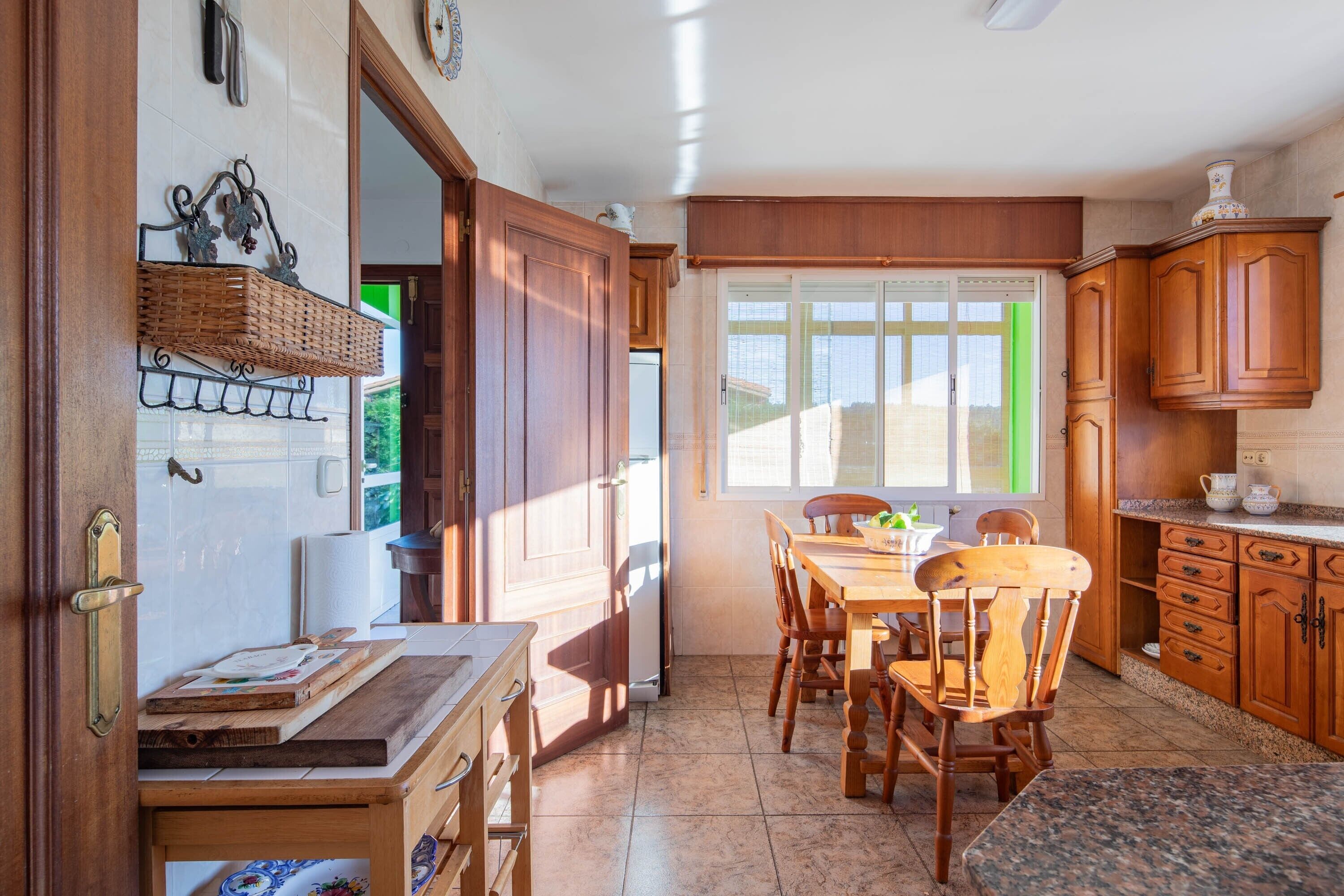Una cocina con armarios de madera, una mesa de comedor, sillas, un refrigerador y una ventana con vistas.