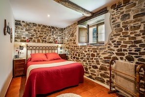 Quarto com parede de pedra, estrutura de cama de madeira, janela com vista e mesa de cabeceira com abajur.