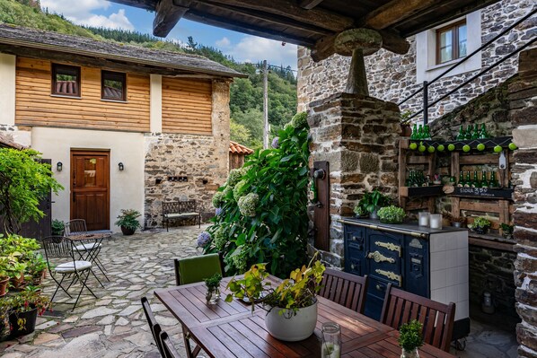 A rustic stone building with a wooden door, a stone staircase, and a bar area with bottles and greenery.