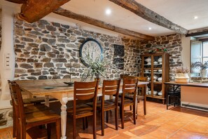 A rustic dining area with a stone wall, wooden table, chairs, and a clock.