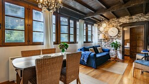 Ein rustikales Interieur mit Esstisch, Korbstühlen, einem blauen Sofa und einer Steinwand mit einer Uhr.