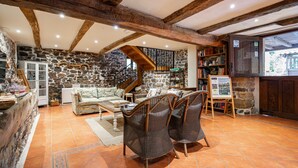 Ein rustikales Interieur mit freiliegenden Holzbalken, Steinwänden, einer Steintreppe, einem Sofa, Korbsesseln und einem Bücherregal.