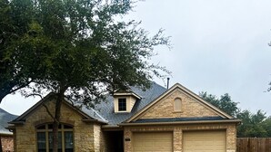 Une maison de plain-pied avec une façade en pierre, un garage et un jardin devant.