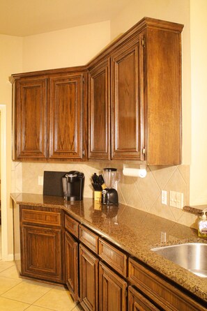 Una cocina con armarios de madera, encimera de granito, cafetera, licuadora y un lavabo.