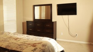 Une chambre à coucher avec un lit, une commode, un miroir et un téléviseur.