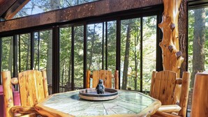 A wooden dining table with chairs, a bear statue, and a glass top. - Riverside Luxury: Hot Tub, Fire Pit & Fishing Dock! Game Room, Fireplace! (Ellijay)