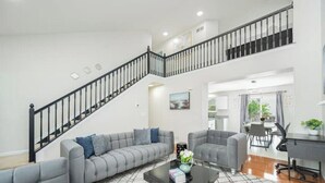Un amplio espacio habitable con un sofá seccional gris, una mesa de centro negra y una escalera con barandillas negras.
