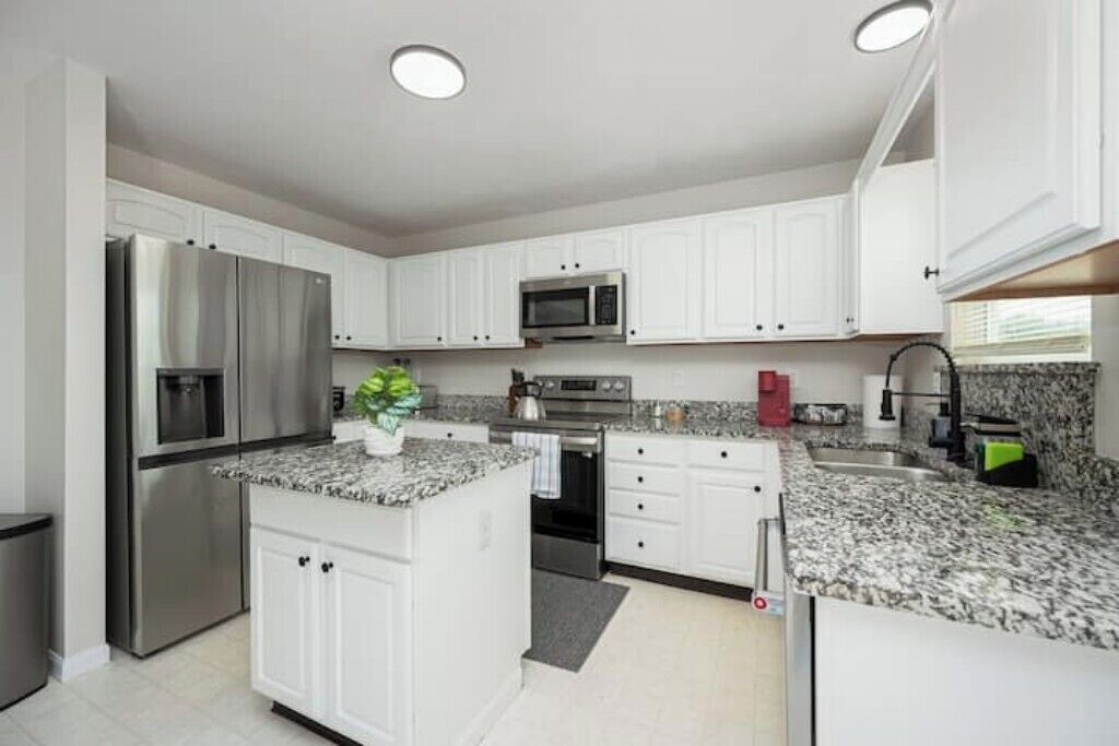 Una cocina moderna con armarios blancos, electrodomésticos de acero inoxidable, encimeras de granito y una isla central.