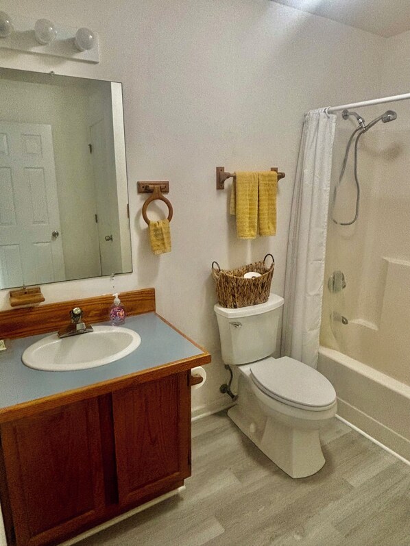 A bathroom with a wooden vanity, a toilet, a shower, and a mirror.
