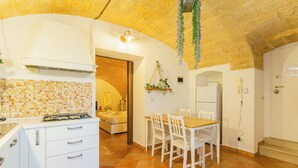Une cuisine avec des meubles blancs, un pare-feu en carrelage et un coin repas comprenant une table et des chaises en bois.