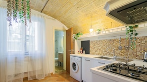 Une cuisine compacte équipée d’un lave-linge, d’une cuisinière et d’un plan de travail carrelé.