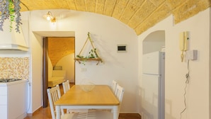 Un coin repas avec une table en bois et des chaises blanches, une plante suspendue, un luminaire fixé au mur et un réfrigérateur blanc.