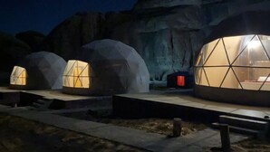 Three geodesic dome structures with internal lighting, set against a rocky cliff backdrop at night. - Suhail Camp (Wadi Rum)