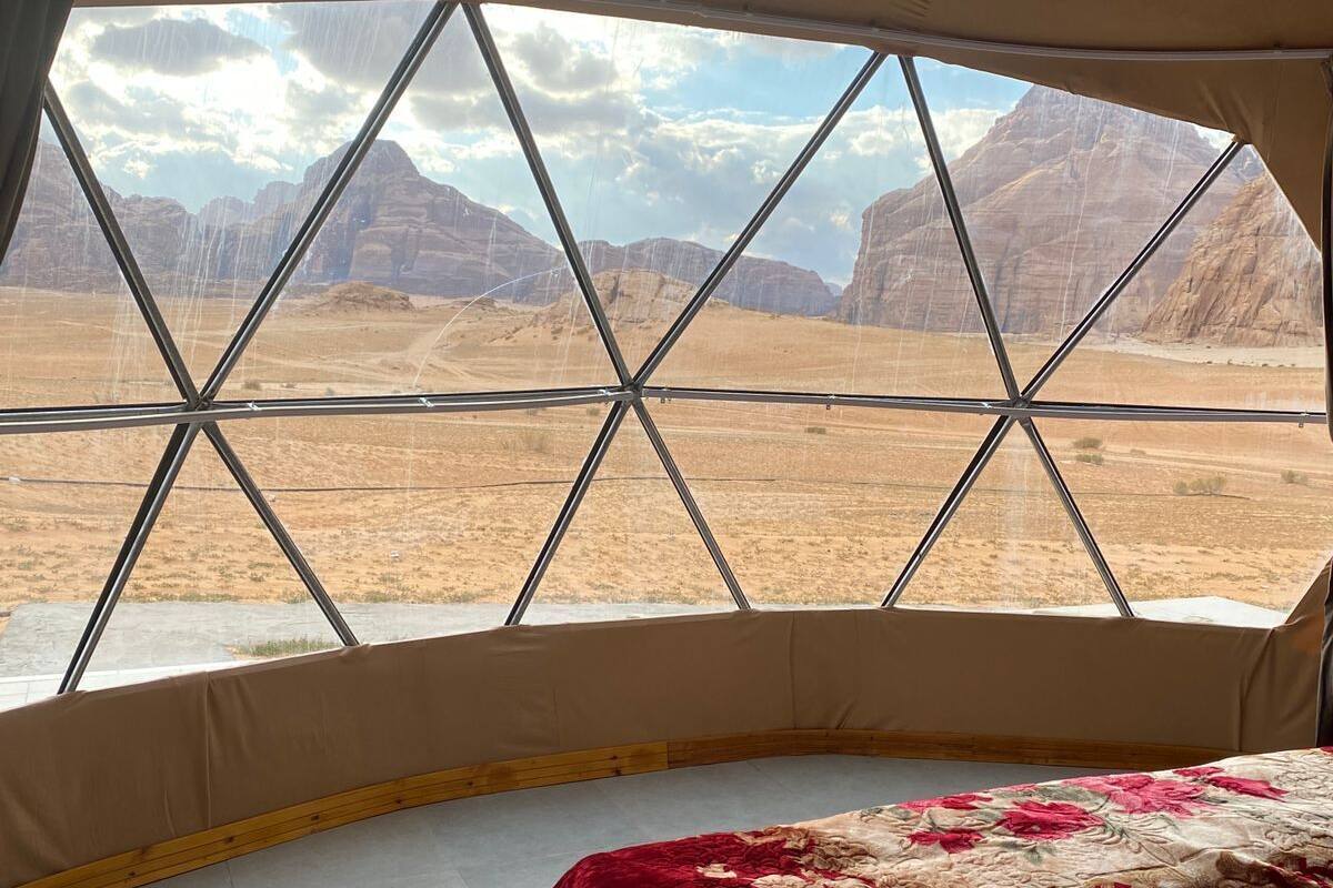 A bed in a tent with a view of a desert landscape.