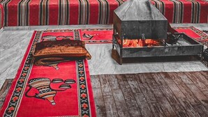 A room with striped red and black walls, a wooden bench, a fireplace, and a patterned rug. - Suhail Camp (Wadi Rum)