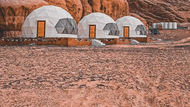 Three dome-shaped yurts with wooden doors, set against a backdrop of reddish rock formations. - Suhail Camp (Wadi Rum)