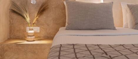 A bedroom with a curved ceiling, a bedside table with a vase of dried plants, and a bed with patterned bedding.