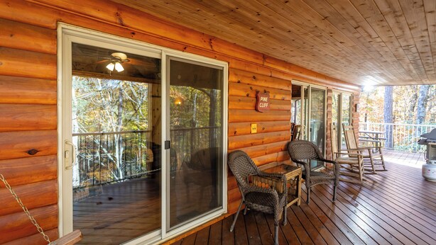 A wooden cabin with a covered porch, sliding glass doors, wicker chairs, and a sign indicating 'Pine Cliff'.
