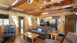 A wooden cabin interior with a sofa, rocking chair, and a kitchen area.