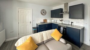 A compact kitchen with dark blue cabinets, a white countertop, and a modern stove. - Welcome to Clementi, your modern holiday retreat in Penrith, Cumbria. (Penrith)