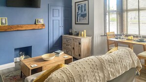 A room with a bed, a wooden dresser, a table with a bowl, a TV mounted on the wall, and a window with blinds. - Welcome to Clementi, your modern holiday retreat in Penrith, Cumbria. (Penrith)