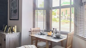 A dining area with a table set for four, wooden chairs, a white cushioned bench, and a window with blinds. - Welcome to Clementi, your modern holiday retreat in Penrith, Cumbria. (Penrith)