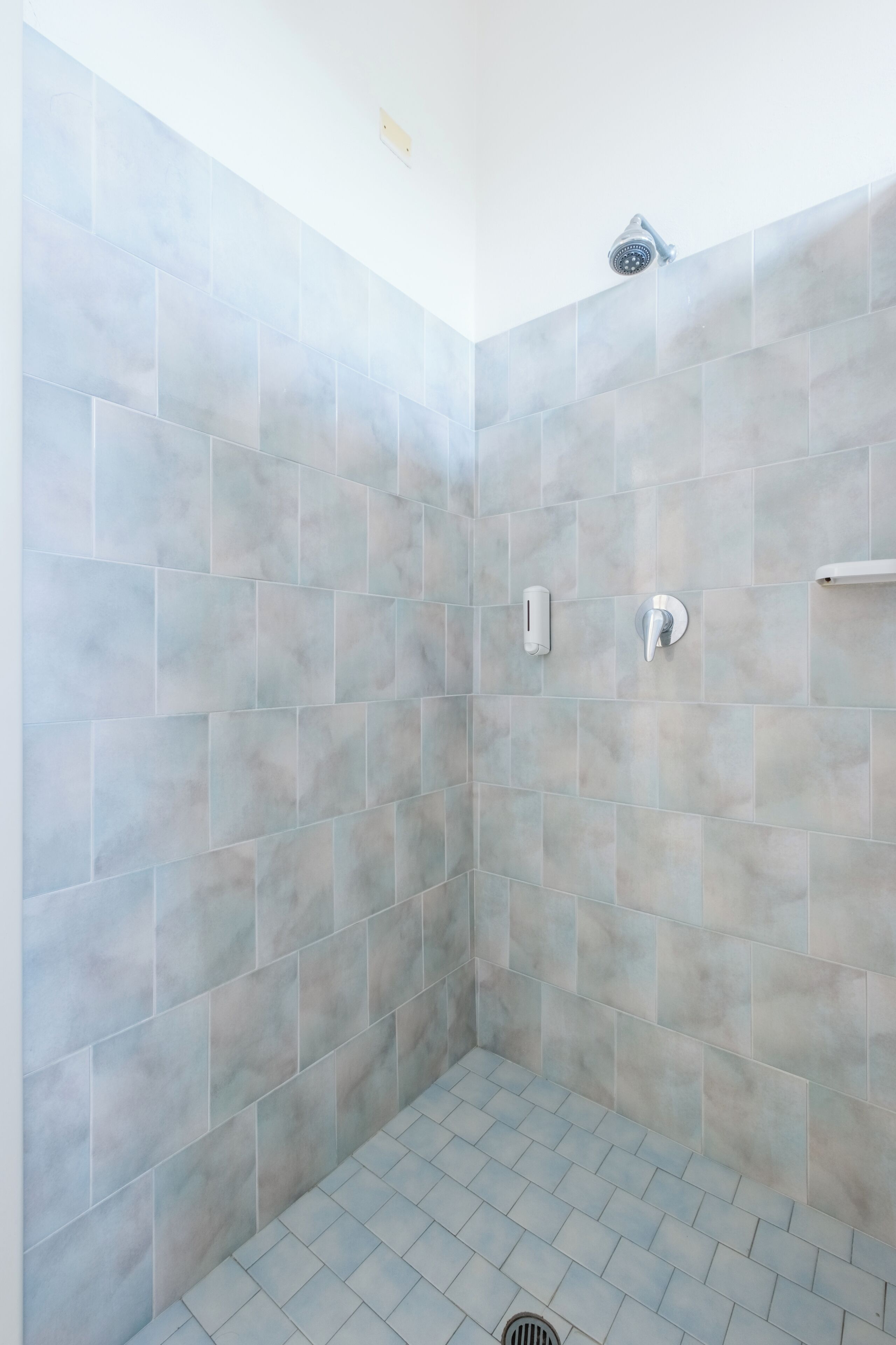 A shower area with grey tiles and a handheld showerhead.