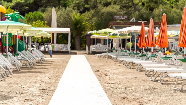A beach with rows of sun loungers and umbrellas, a white pathway, and a building in the background. - Meet Hostel Cervia (Cervia)