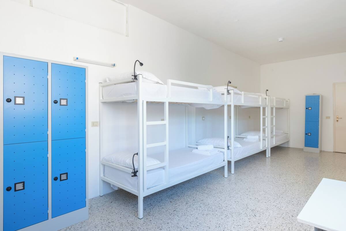 A dormitory room with bunk beds, a desk, and blue lockers.