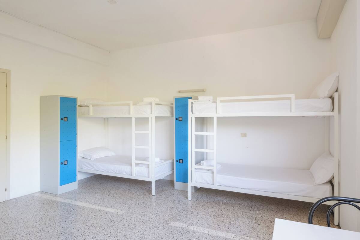 A dormitory room with bunk beds, a blue storage unit, and a white desk.