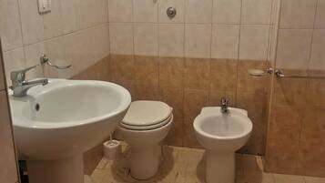 A bathroom with a sink, toilet, and bidet, tiled walls, and a window above the sink.