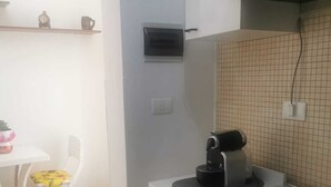 Een compacte keuken met een gasfornuis, een koffiezetapparaat en een kleine eethoek met een stoel en tafel.