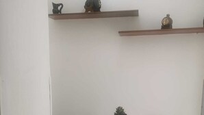 Een kleine witte tafel met twee witte stoelen, elk met een geel kussen met zonnebloemen. Daarboven bevinden zich twee houten planken met decoratieve objecten.