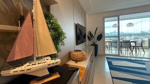 A modern living room with a sailboat model, a plant, and a view of the city through large windows. - Enseada Azul - Beachfront, Luxury (Guarapari)